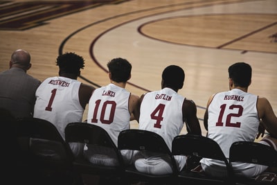 四名篮球运动员坐在篮球场的另一个人旁边
